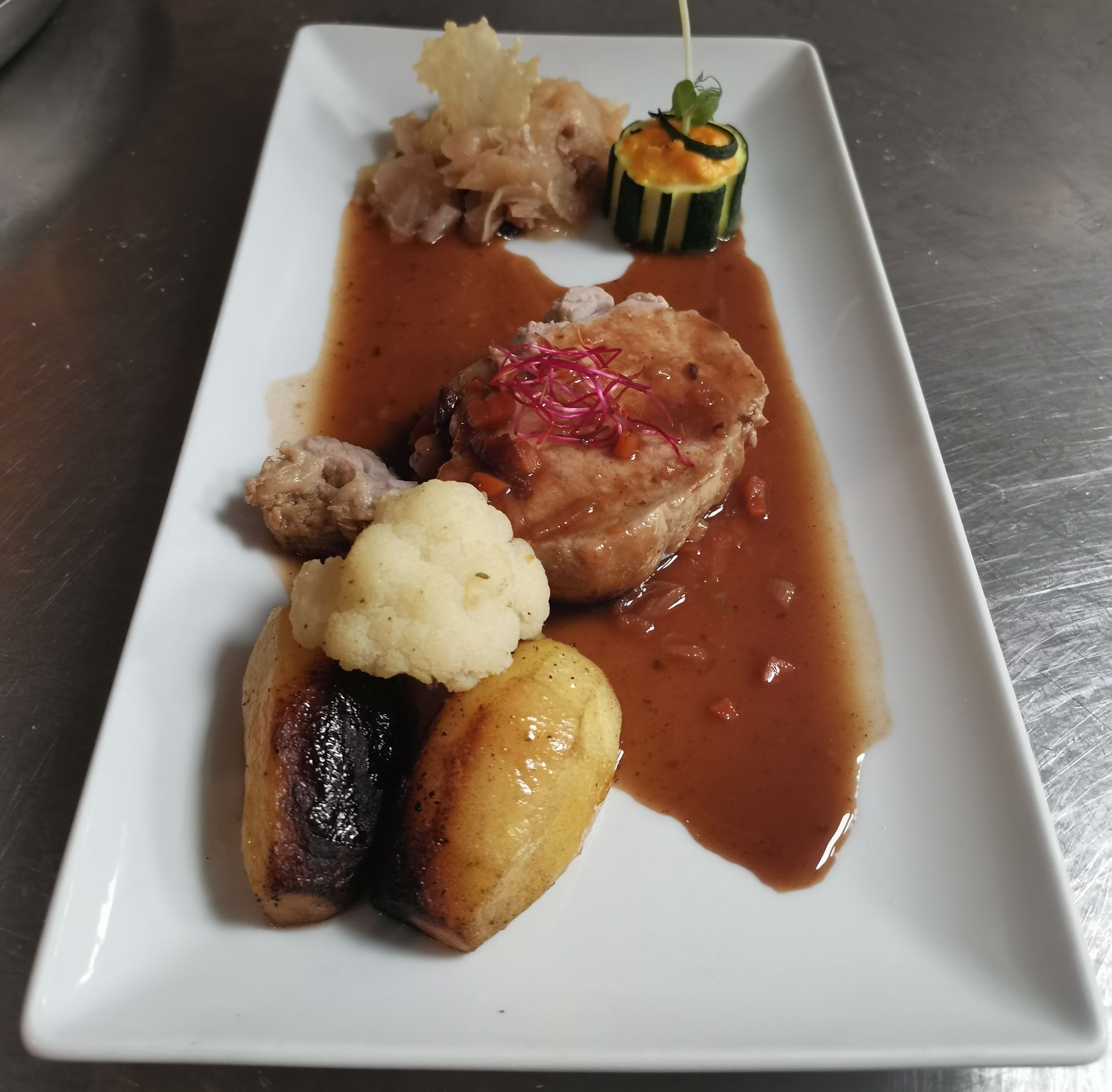 Un repas à l'assiette composé d'une coupe de viande avec sauce, pommes de terre rôties, chou-fleur et garnitures