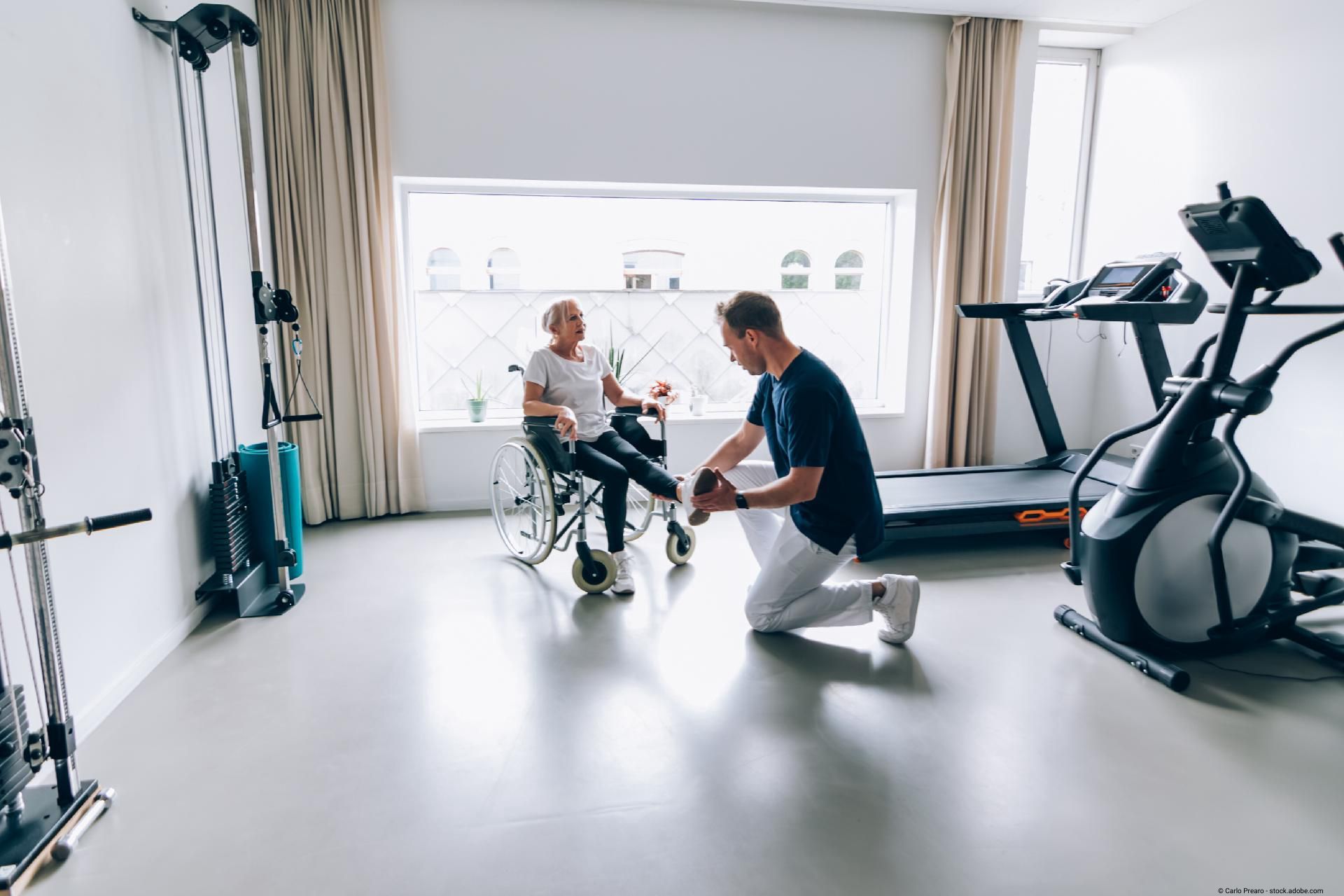 Therapeut unterstützt älteren Mann im Rollstuhl bei einer Übung im Rehabilitationsraum.
