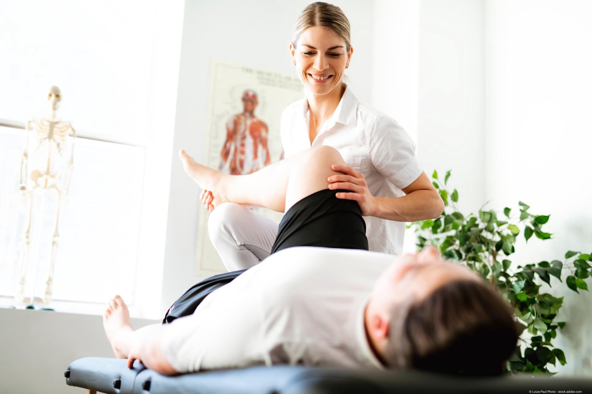 Physiotherapeutin mobilisiert das Bein eines liegenden Patienten während einer Behandlung.