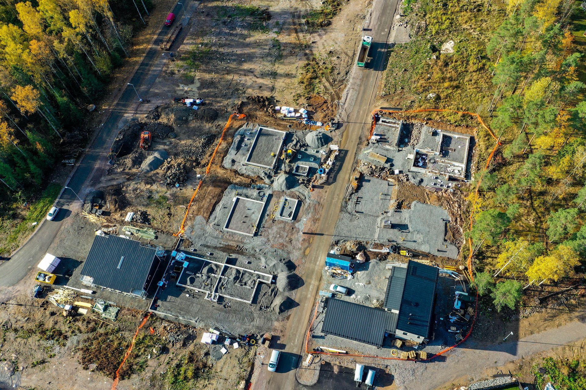 Ilmakuva asuinrakennustyömaasta, jossa näkyy rakennuksen perustuksia, runkoa ja laitteita metsäisellä alueella.