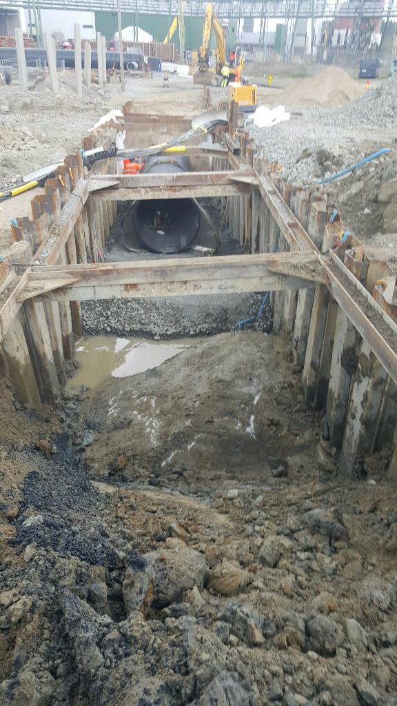 Suuri musta putki on syvässä kaivetussa ojassa terästukien tuella aktiivisella rakennustyömaalla.