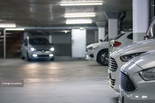 Parking souterrain avec des voitures garées et des néons puissants au plafond.