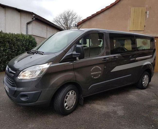 Minibus gris foncé garé à l'extérieur, à côté de bâtiments, par temps nuageux