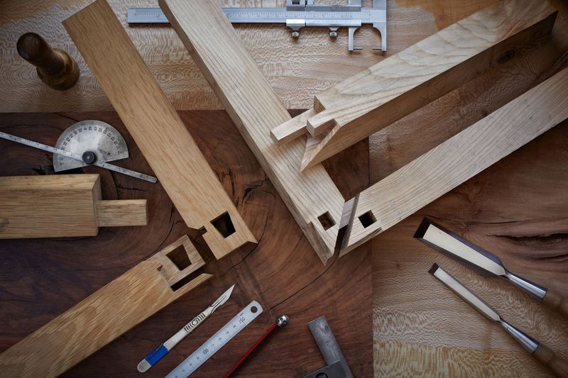 Outils de menuiserie et pièces de bois disposés sur un établi, comprenant une scie, une règle et des serre-joints.