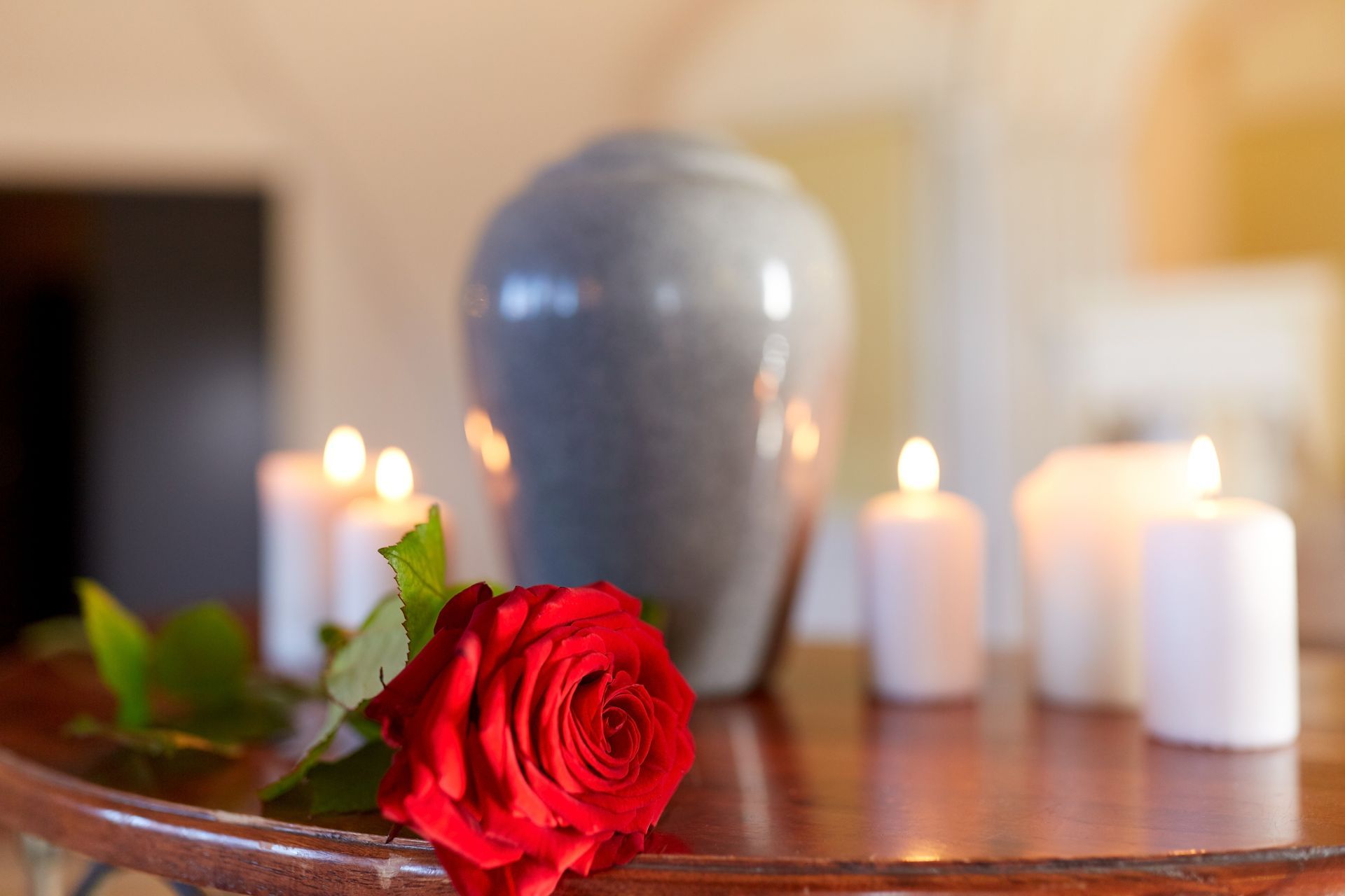 Rose rouge et bougies allumées sur une table en bois, avec un vase gris en arrière-plan.