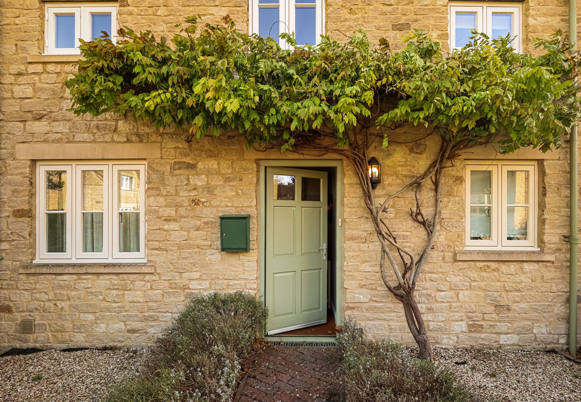 Façade de maison en pierre avec porte verte, balcon couvert de vigne et deux fenêtres de chaque côté
