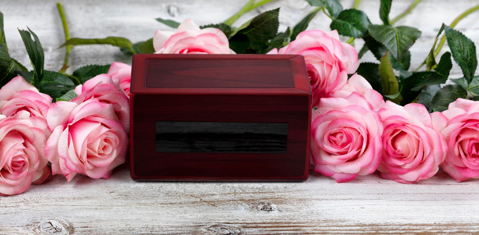 Boîte à souvenirs rouge entourée de roses roses sur une surface en bois blanc rustique.