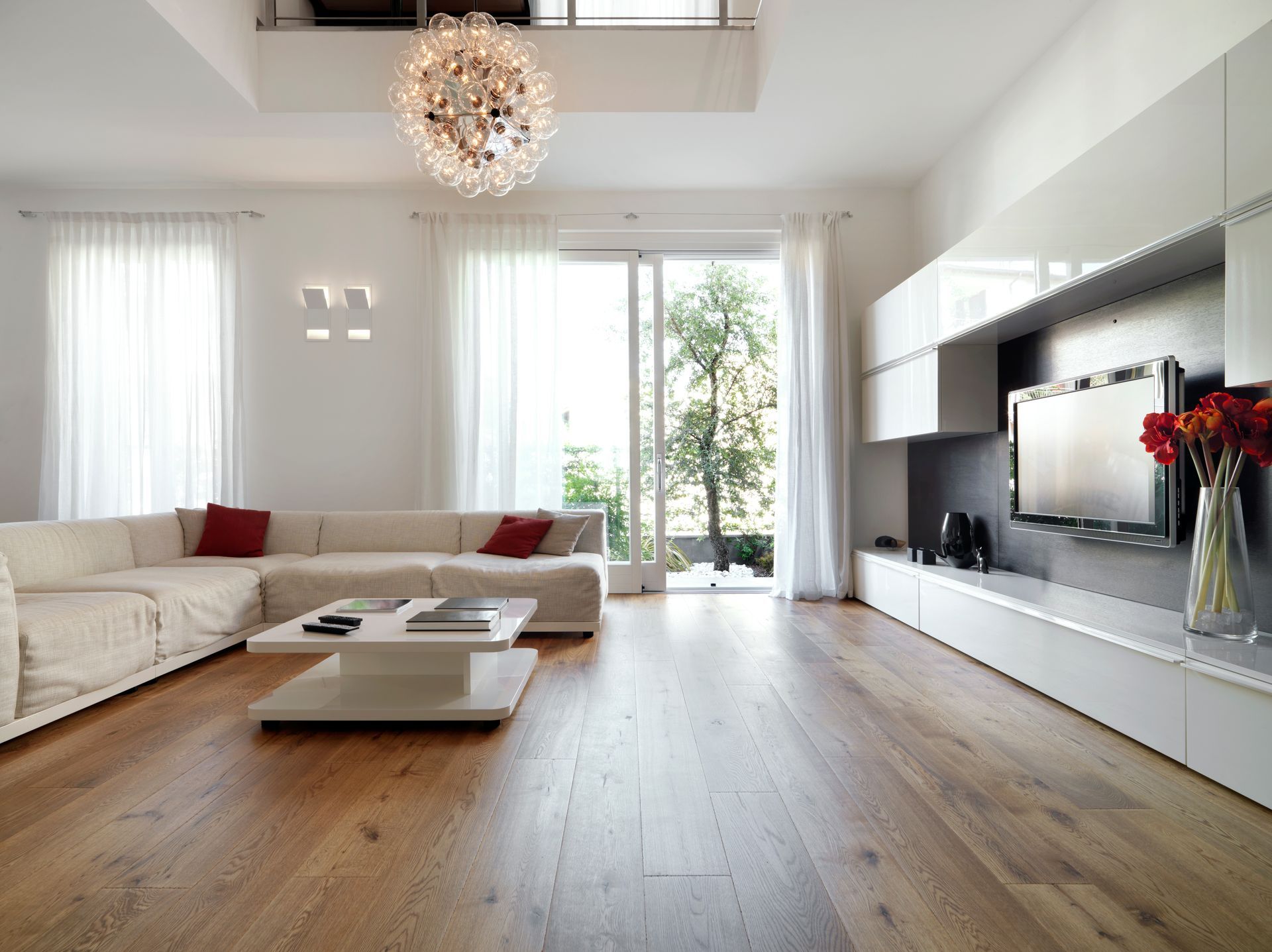 Salon moderne et lumineux avec canapés blancs, parquet clair, grandes fenêtres et télévision murale