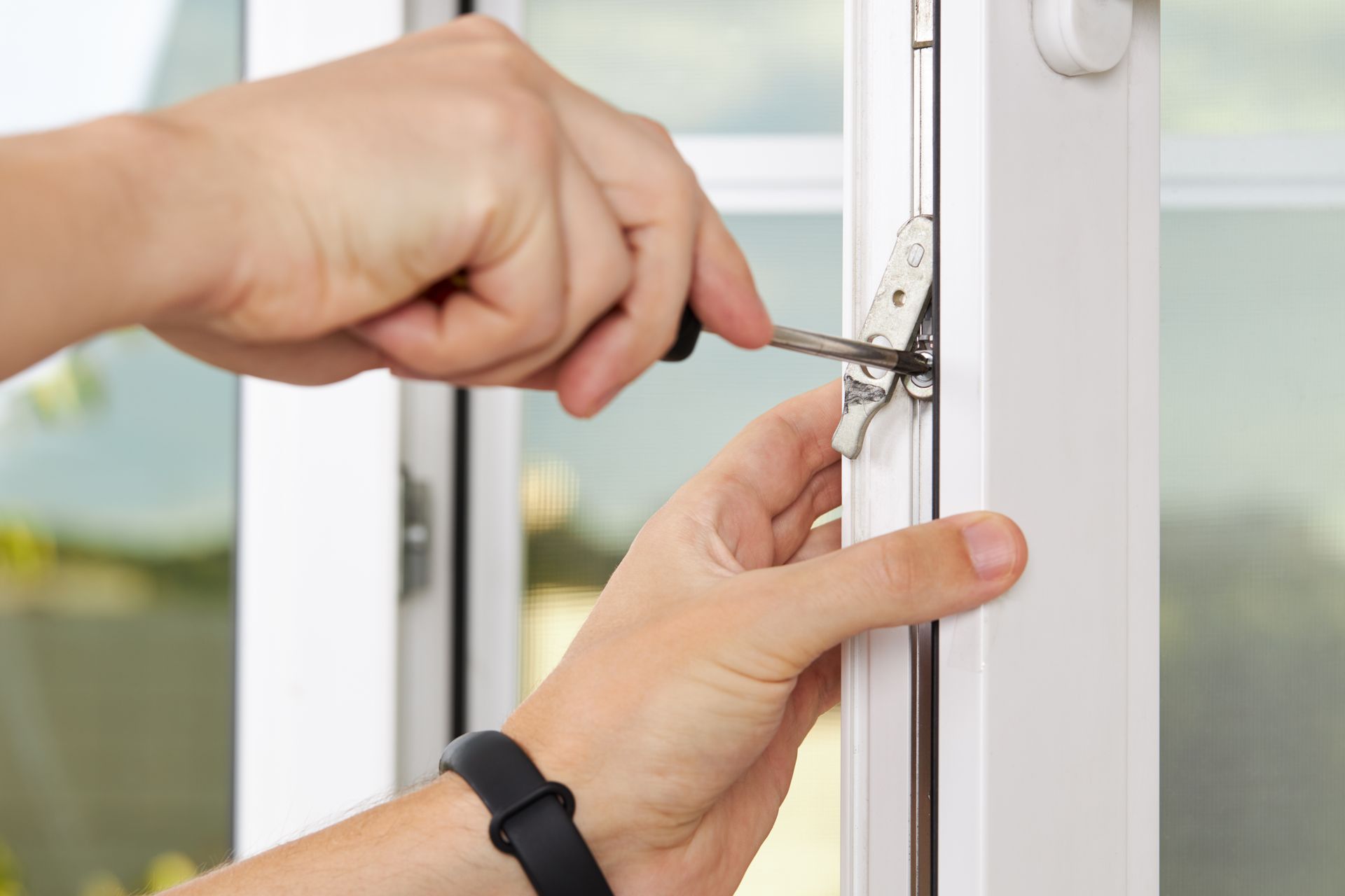 Des mains utilisent un tournevis pour ajuster le loquet d'une fenêtre blanche