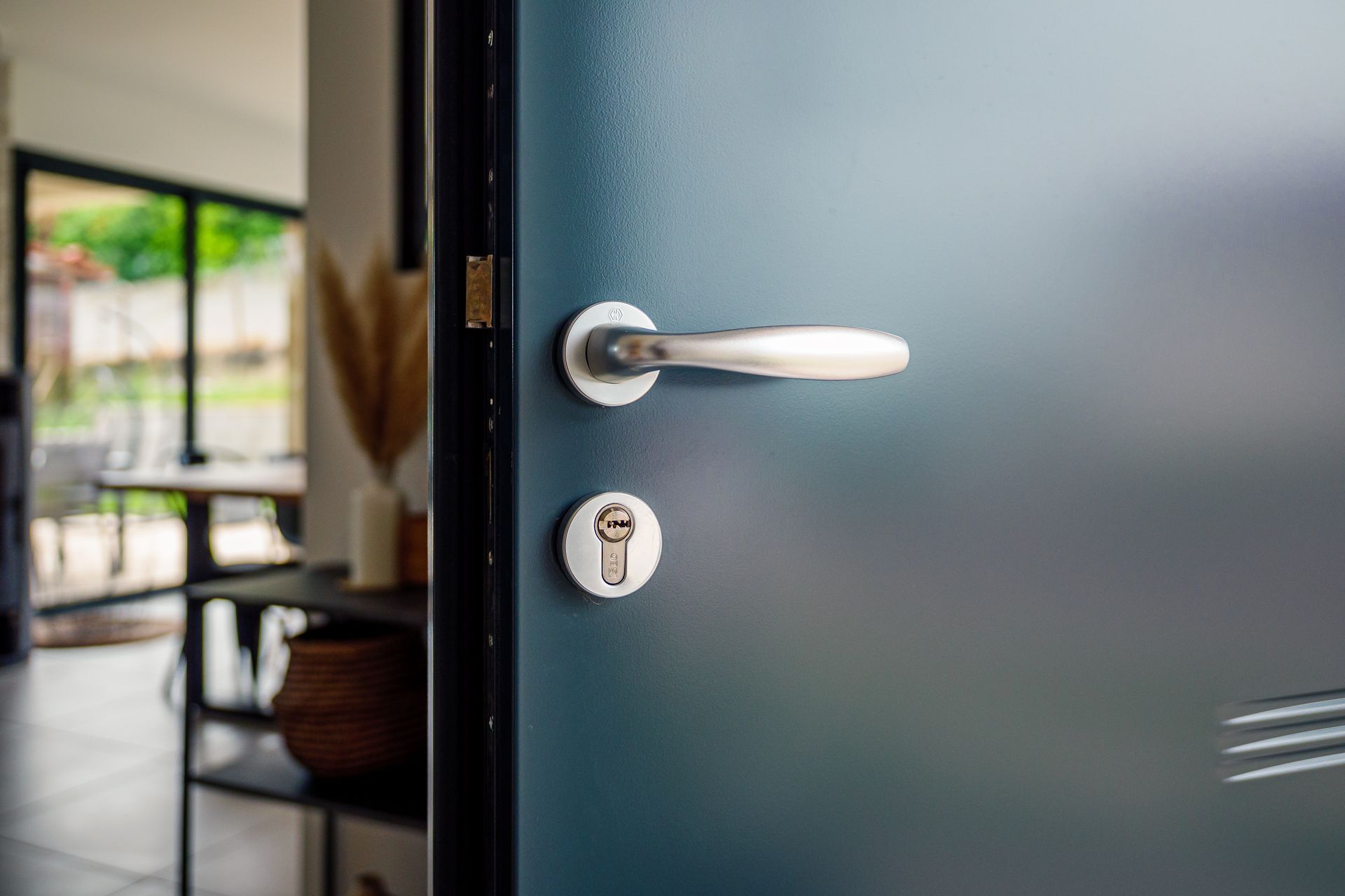 Porte en verre dépoli partiellement ouverte avec poignée argentée, laissant entrevoir une vue floue entre l'intérieur et l'extérieur.