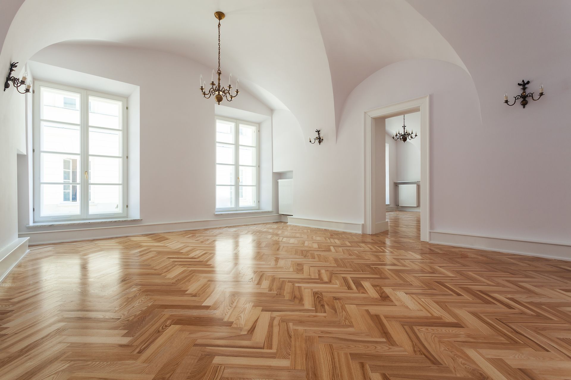 Pièce lumineuse et vide avec parquet à chevrons, murs blancs, plafond voûté et grandes fenêtres