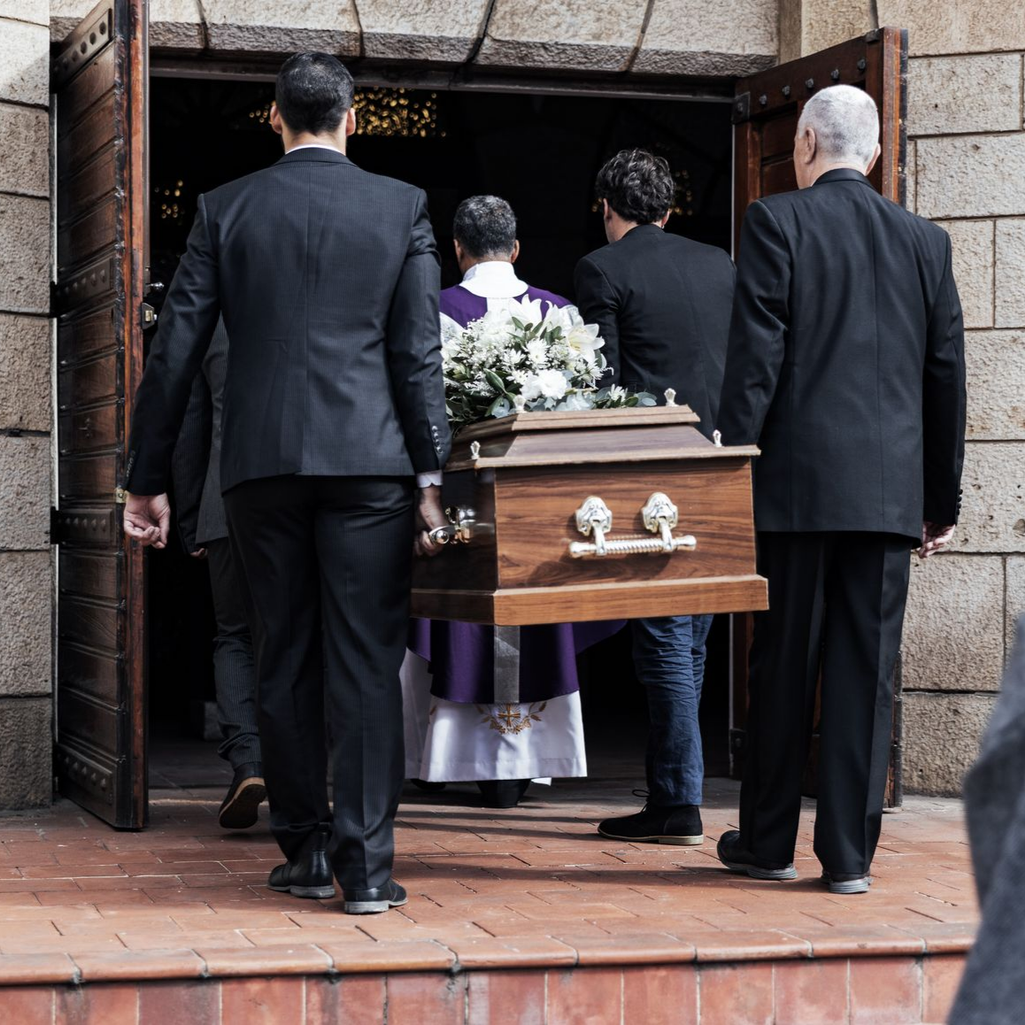 Des personnes en deuil portent un cercueil dans une église, précédées d'un officiant vêtu de violet.