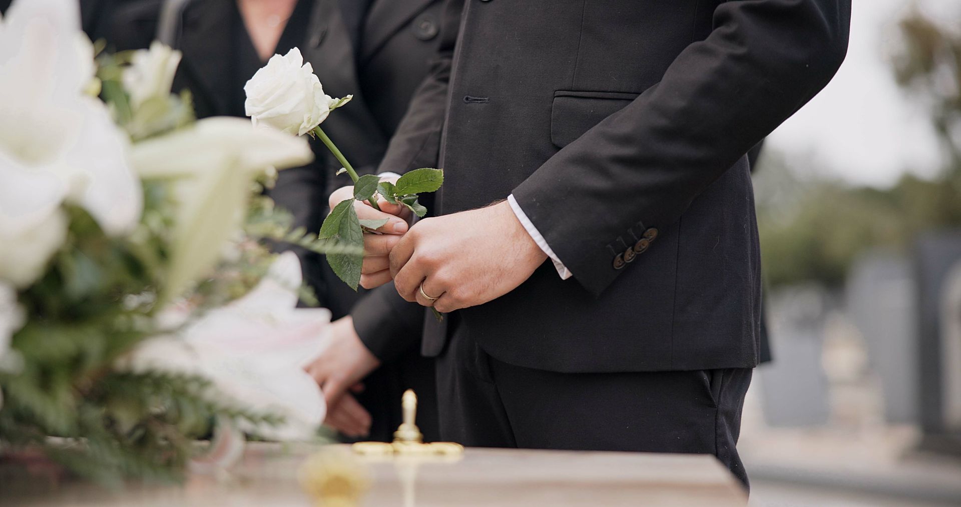 Une personne en costume noir tenant une rose rouge lors d'une cérémonie funéraire
