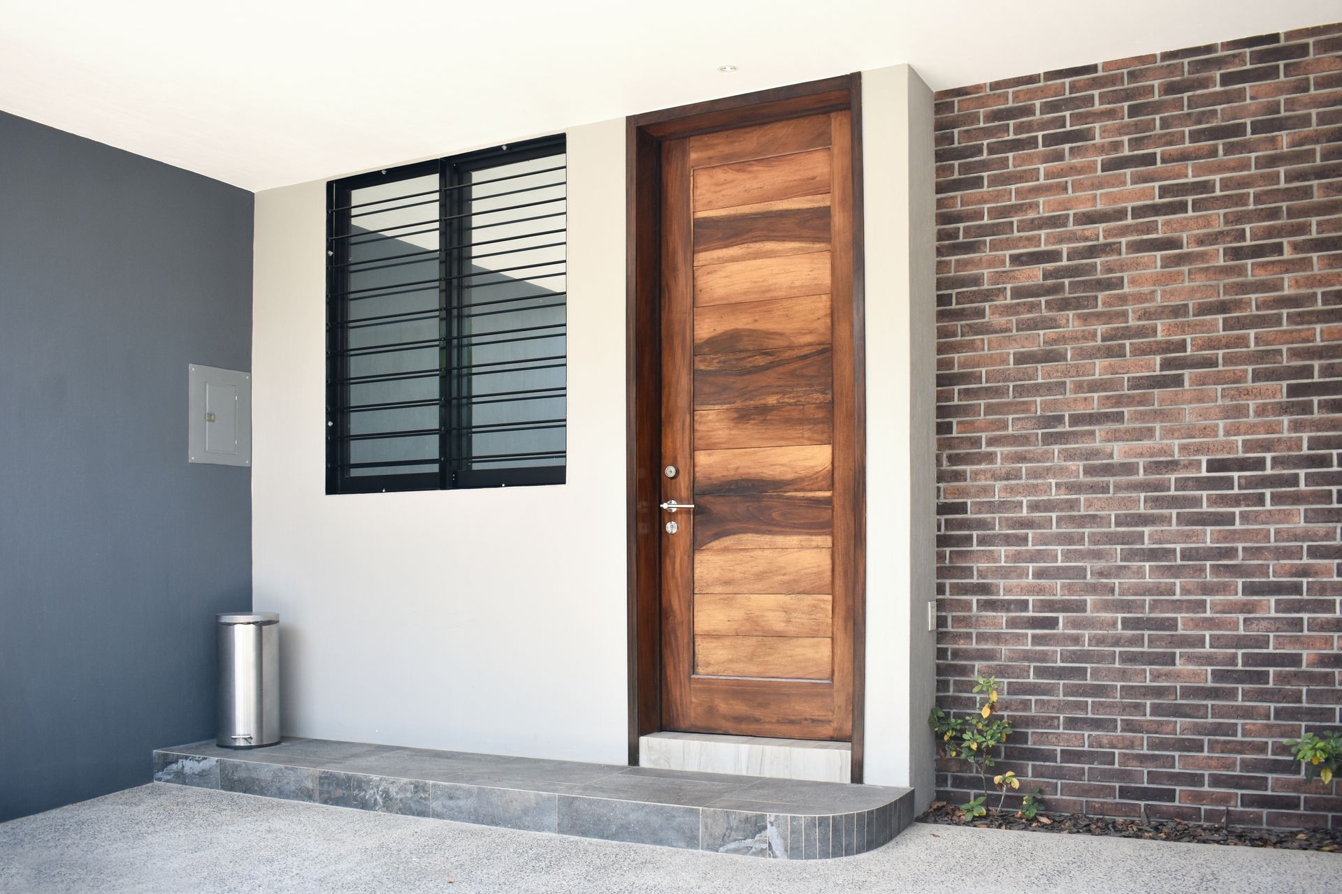 Entrée de maison moderne avec porte en bois, fenêtre, mur en briques et petites marches en béton