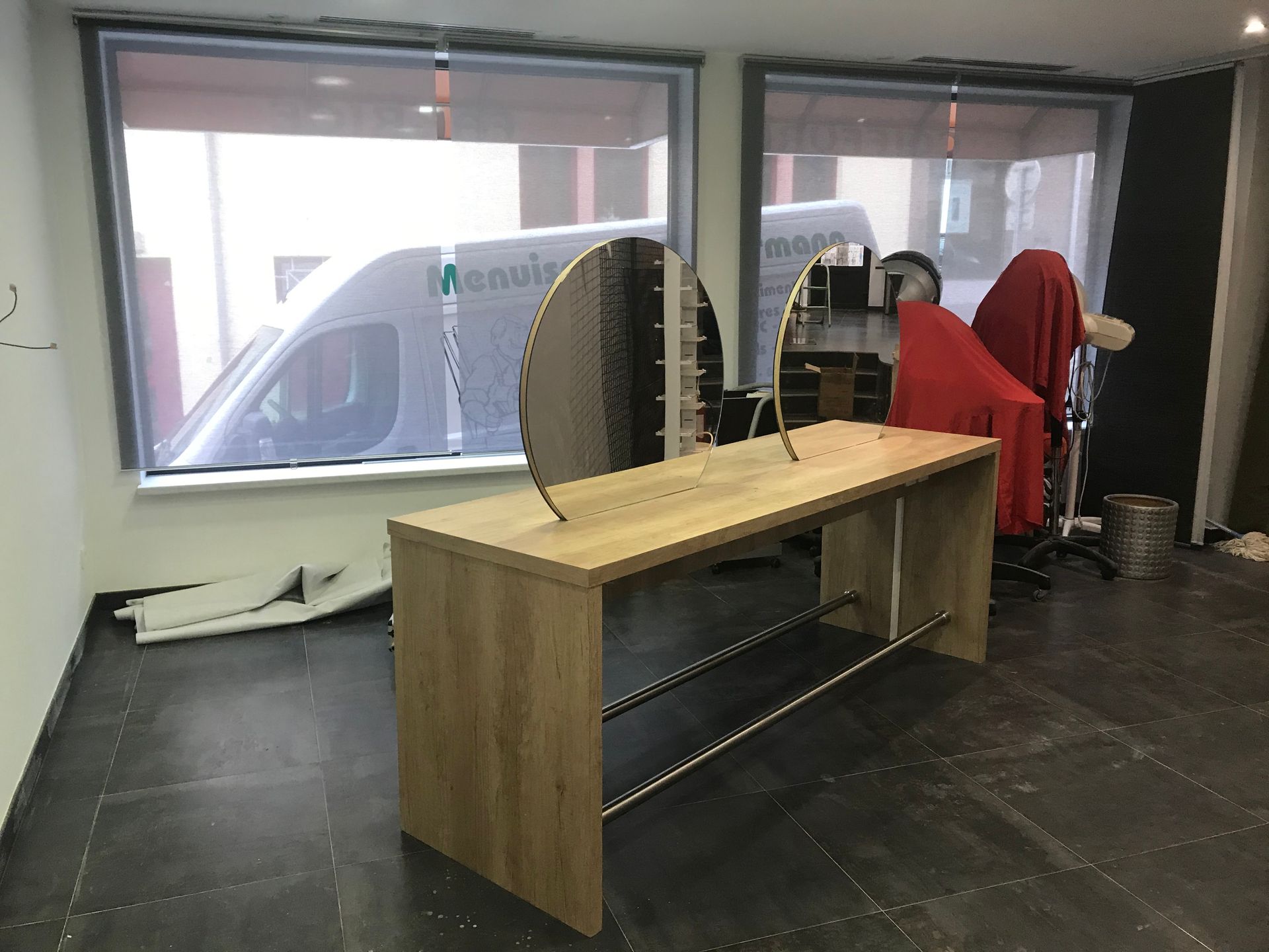 Bureau avec un bureau en bois, un sol carrelé noir, de grandes fenêtres et une chaise rouge en arrière-plan