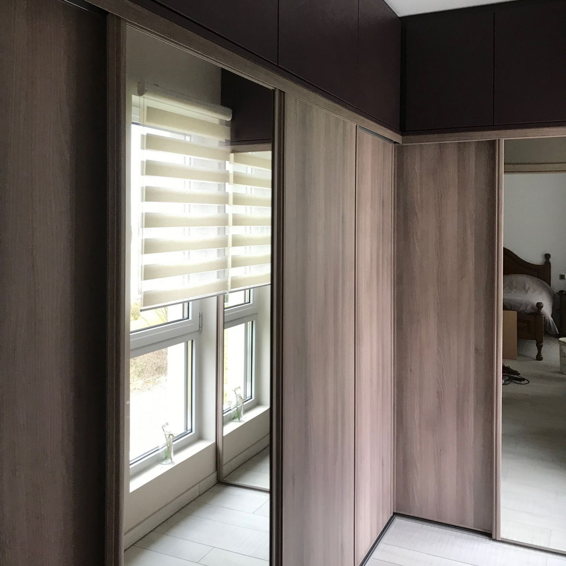 Chambre moderne avec de grandes fenêtres, des stores zébrés et des placards intégrés en bois avec portes miroir.