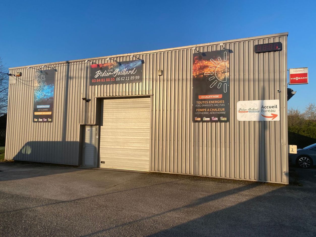 Par temps clair, un entrepôt en métal gris clair présente deux affiches verticales, une porte sectionnelle centrale et une enseigne.