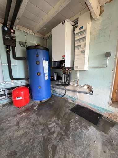 Une buanderie comprenant un grand réservoir d'eau bleu, une chaudière murale blanche, un vase d'expansion rouge et un tableau électrique.