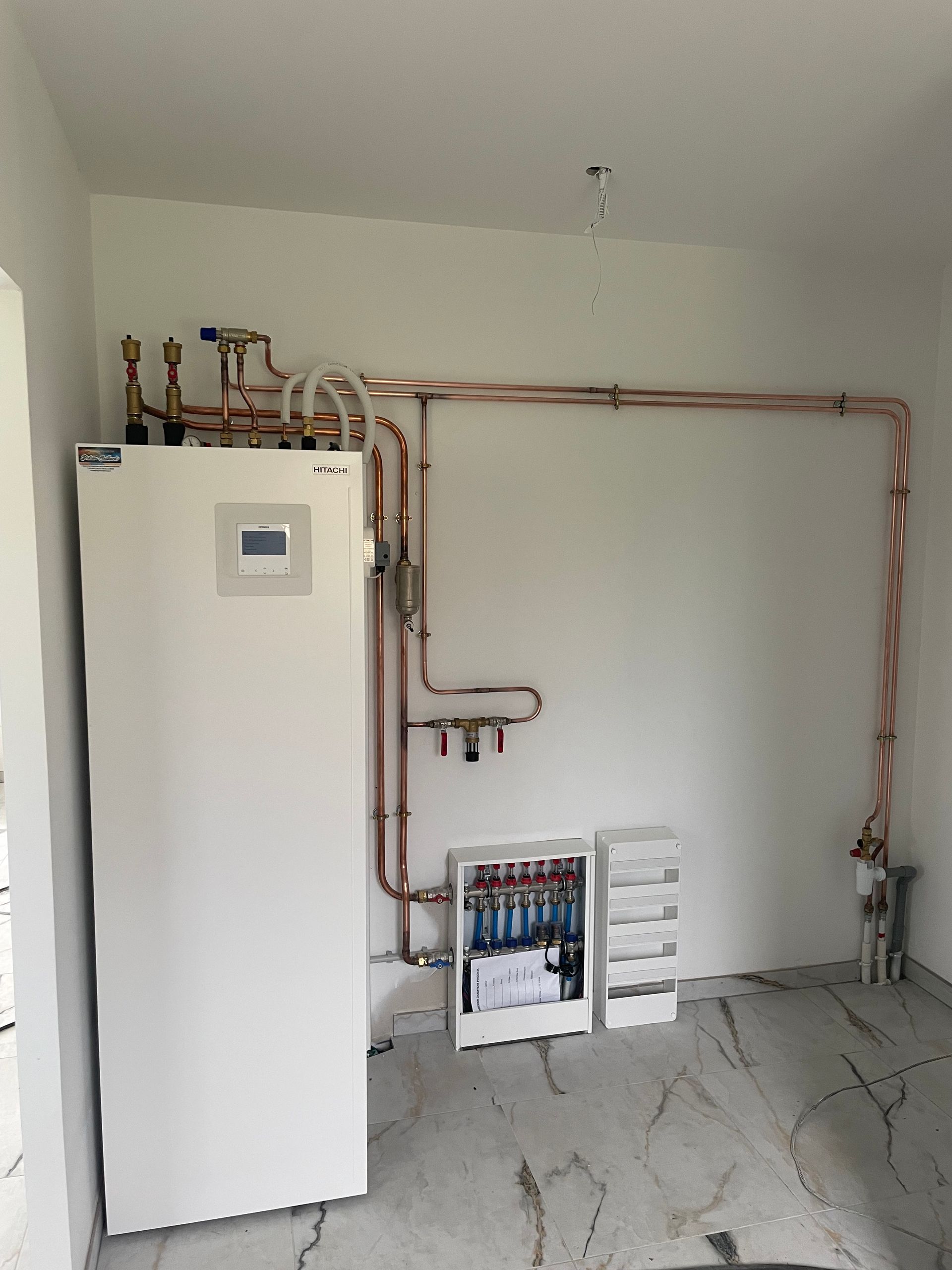 Une chaudière utilitaire blanche se dresse dans une pièce où des tuyaux de cuivre longent le mur blanc jusqu'à un collecteur de chauffage.