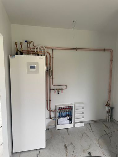Une chaudière utilitaire blanche se dresse dans une pièce où des tuyaux de cuivre longent le mur blanc jusqu'à un collecteur de chauffage.