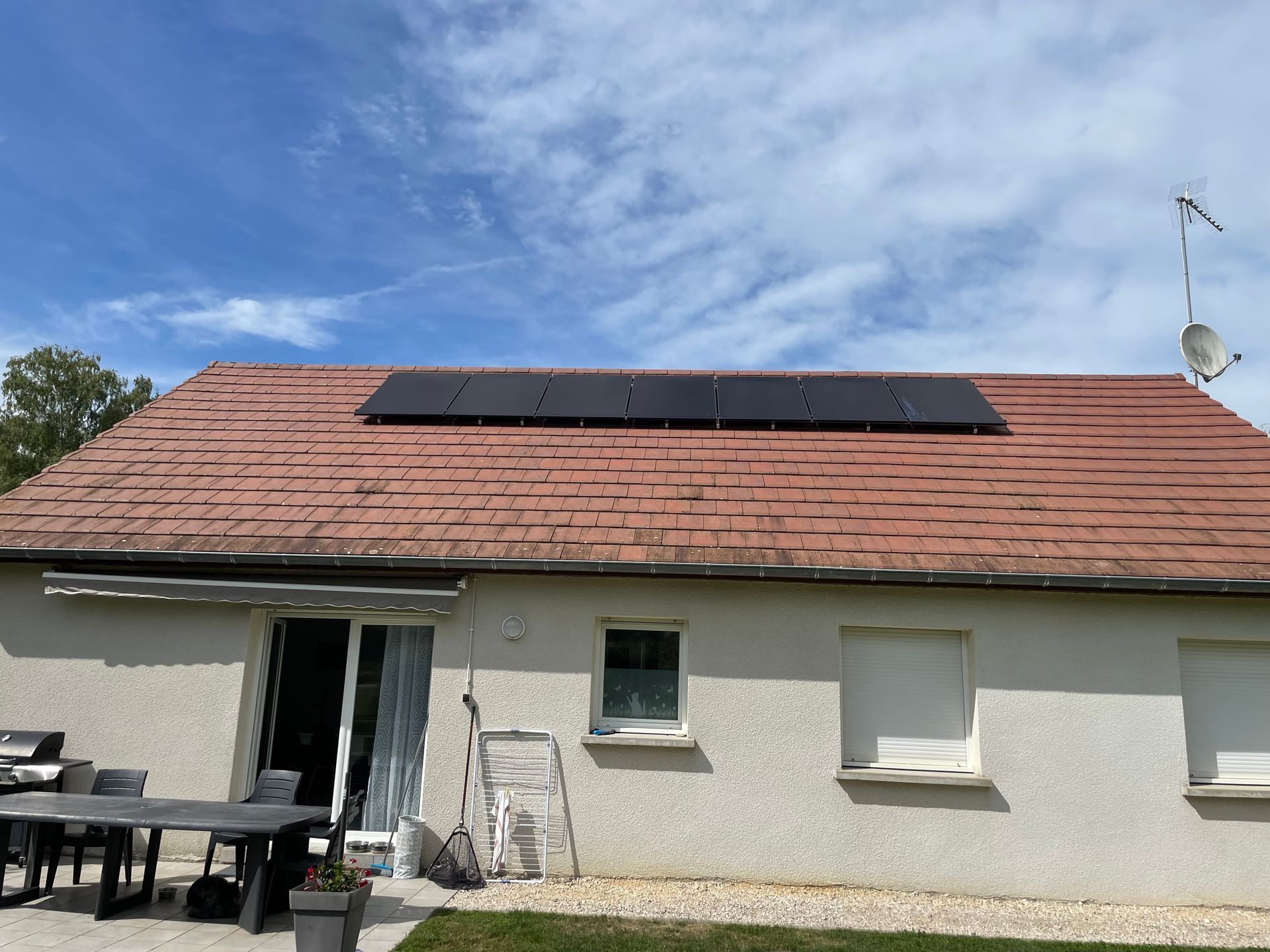 Une maison au toit de tuiles rouges ornée d'une rangée de panneaux solaires, sous un ciel bleu azur.