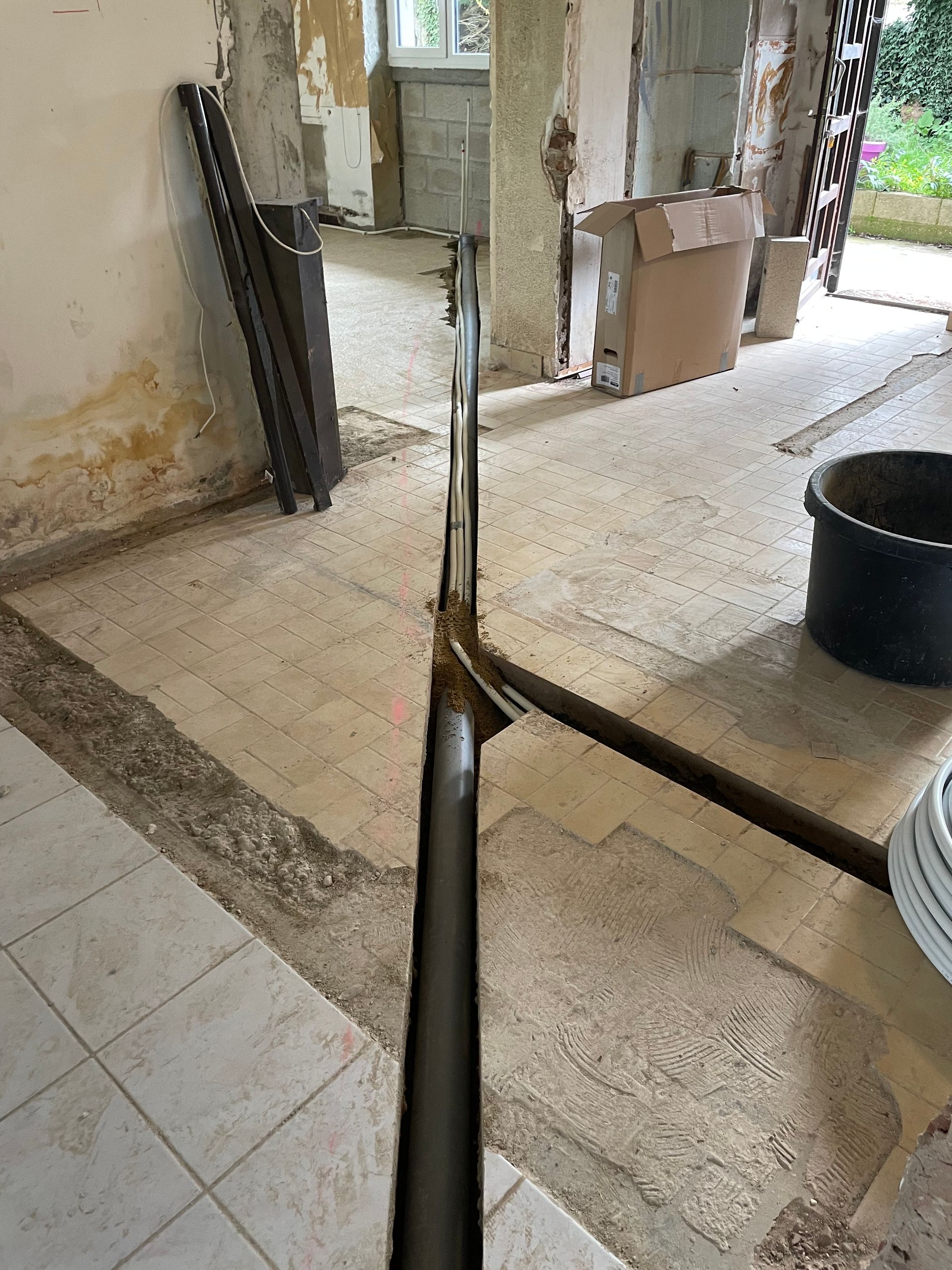 Un assemblage de tuyauterie métallique en forme de T installé sur un sol carrelé dans une pièce en cours de rénovation.