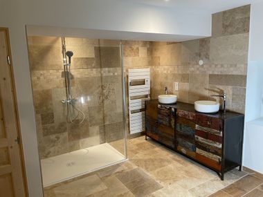 Une salle de bains moderne comprenant une douche à l'italienne avec paroi de verre, un porte-serviettes chauffant blanc et un meuble-lavabo à deux vasques.
