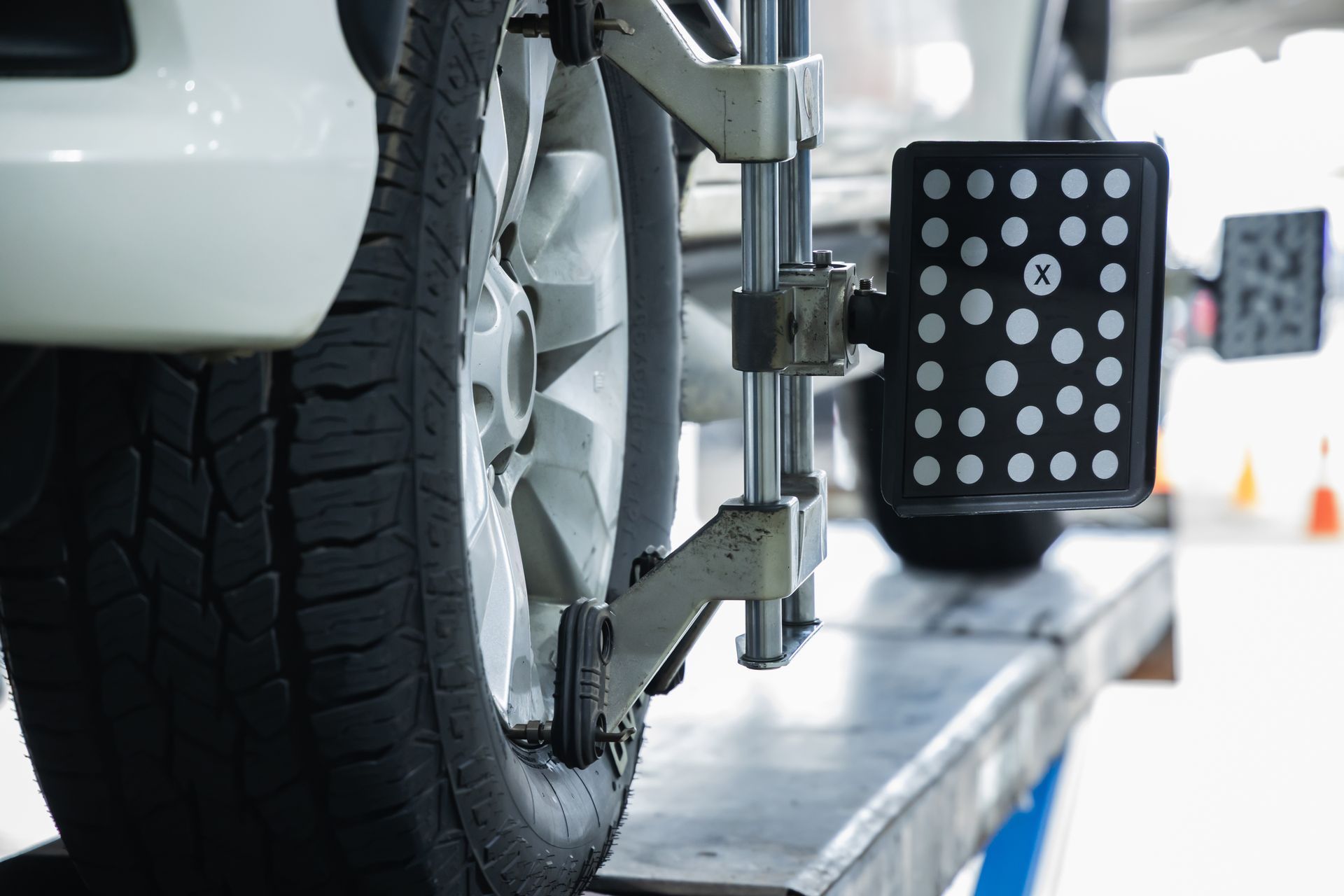 Roue de voiture sur un banc de géométrie dans un garage lumineux, avec un panneau de capteurs à côté du pneu