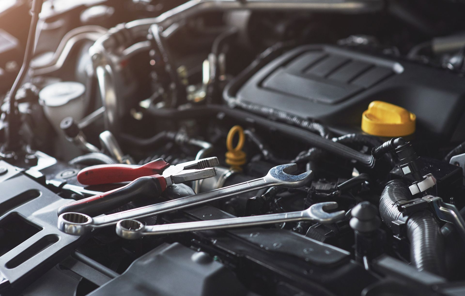 Outils de mécanicien sur un moteur de voiture, avec des clés rouges et argentées et un bouchon jaune visibles.