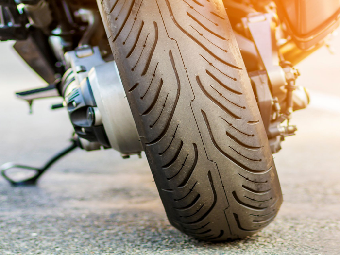 Gros plan sur le pneu avant d'une moto sur le bitume, baigné par un halo de soleil.