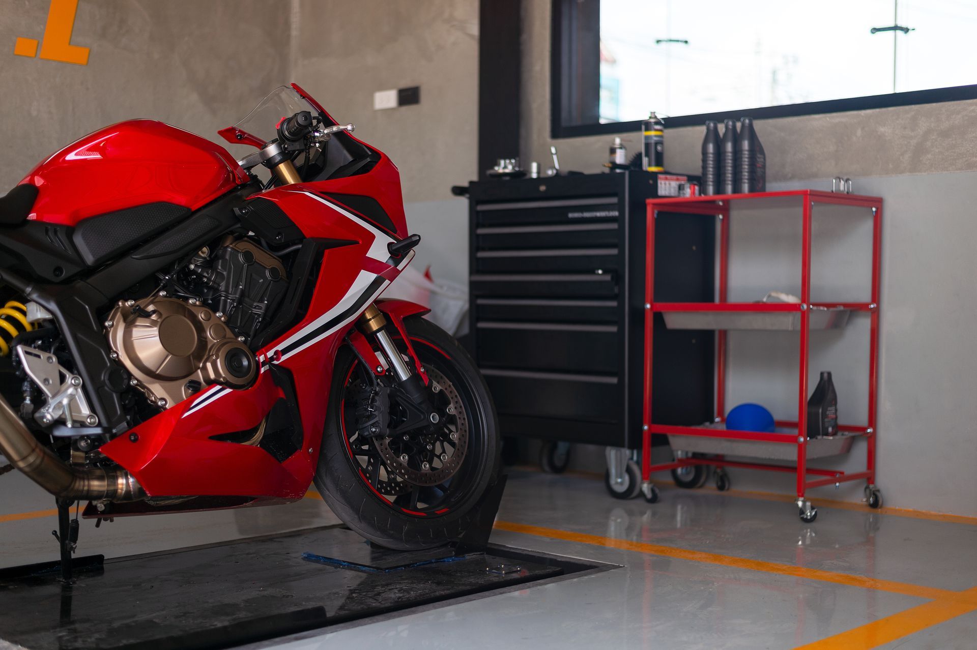 Une moto sport rouge dans un garage, à côté d'une caisse à outils noire et d'un chariot rouge.