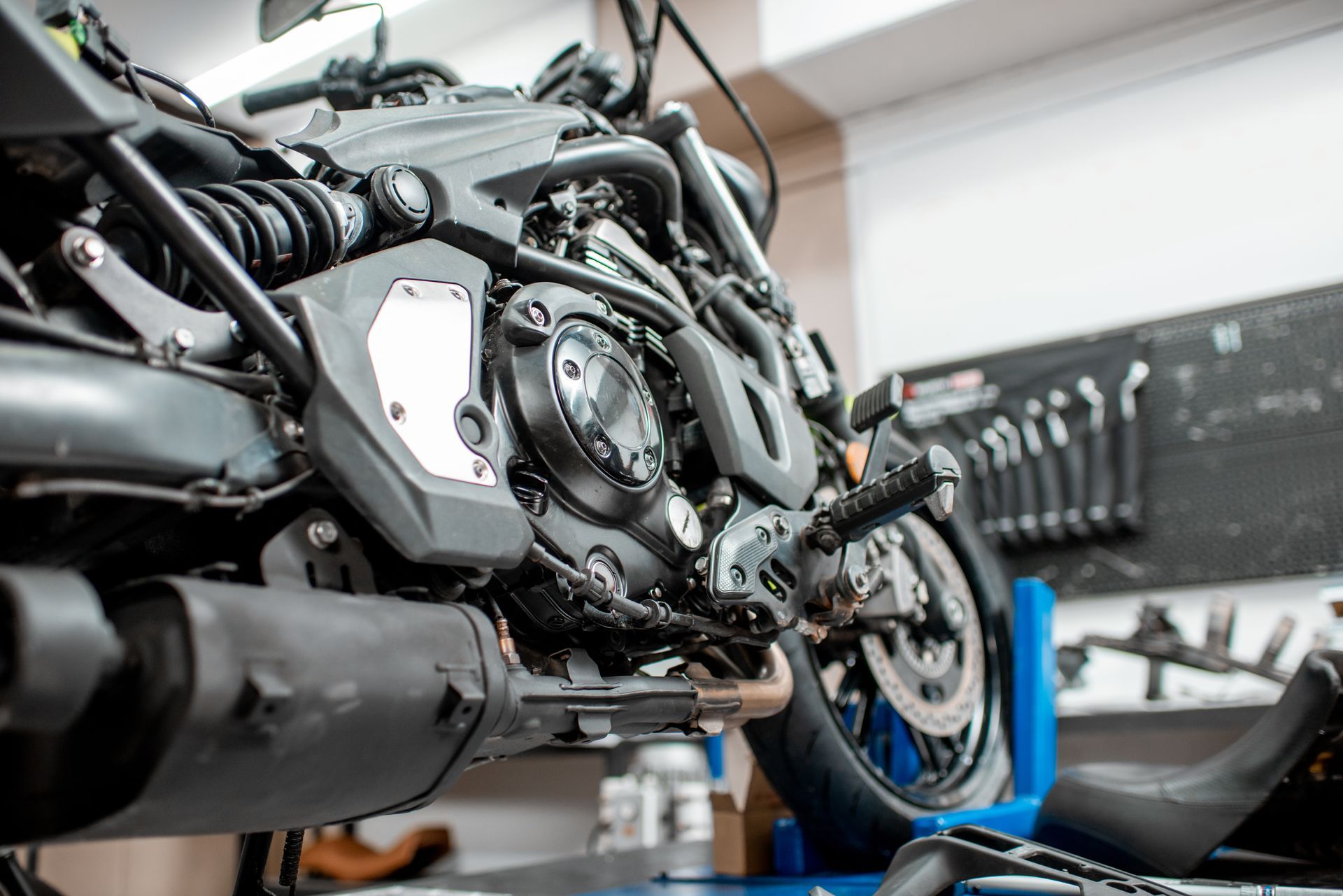 Gros plan sur le moteur et la roue arrière d'une moto dans un atelier, avec des outils et de l'équipement en arrière-plan.