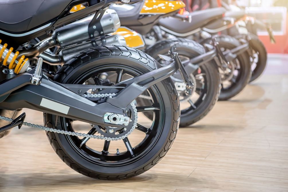 Rangée de motos noires et orange garées à l'intérieur, vue depuis les roues arrière.