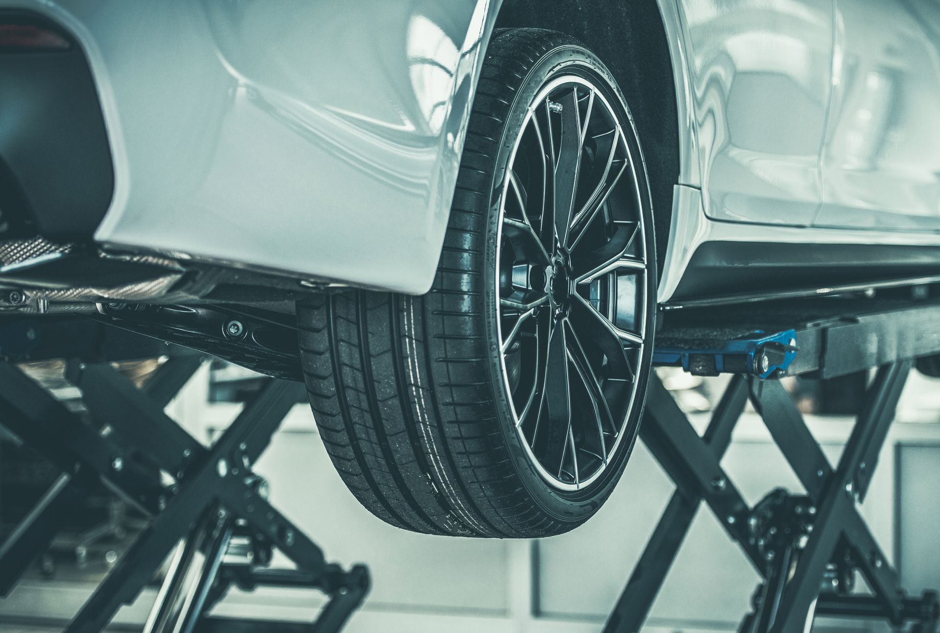 Voiture soulevée par des crics à ciseaux, montrant une roue avant et le dessous de caisse dans un atelier