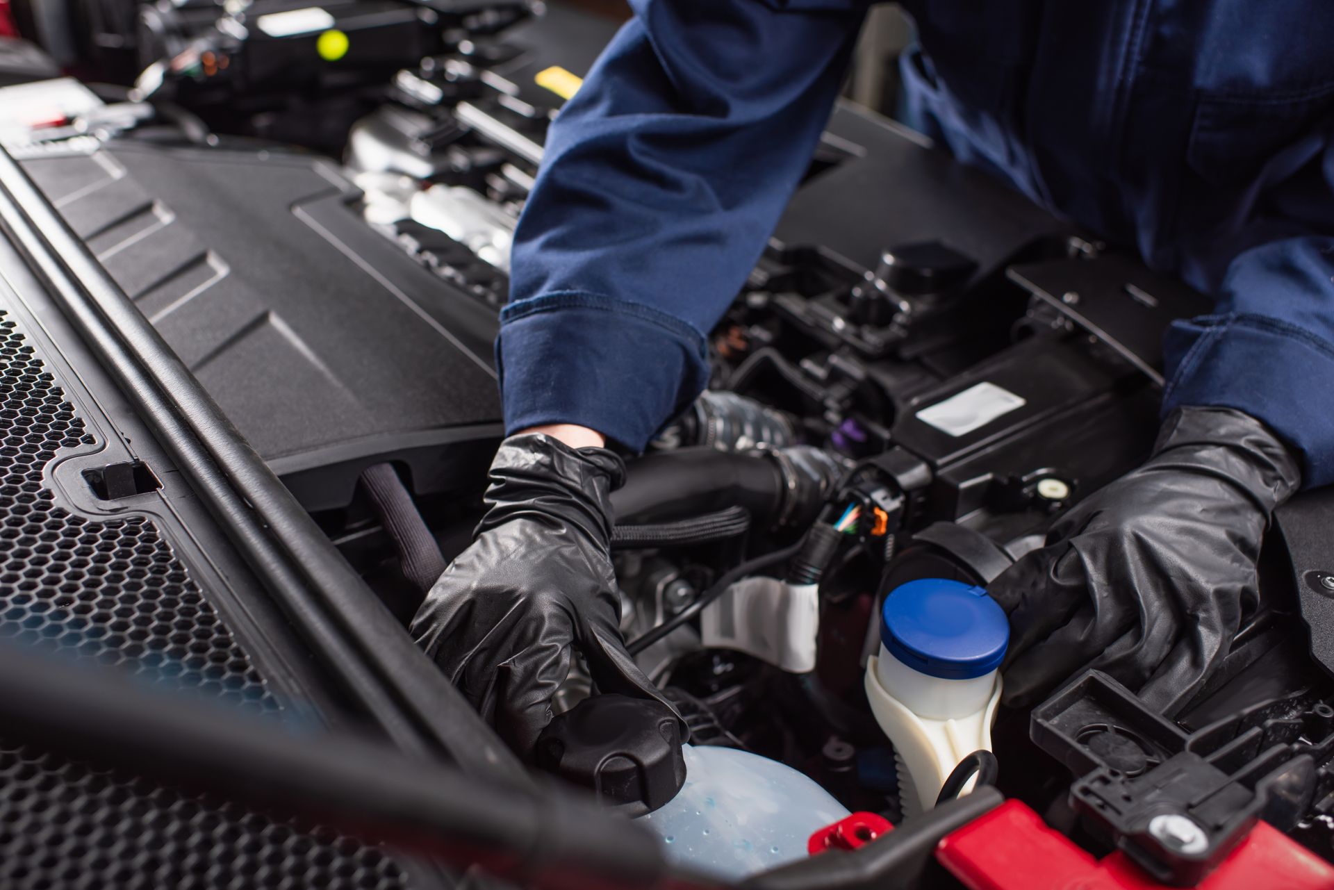 Un mécanicien portant des gants noirs travaille sous le capot d'une voiture, vérifiant les composants et les fluides du moteur.