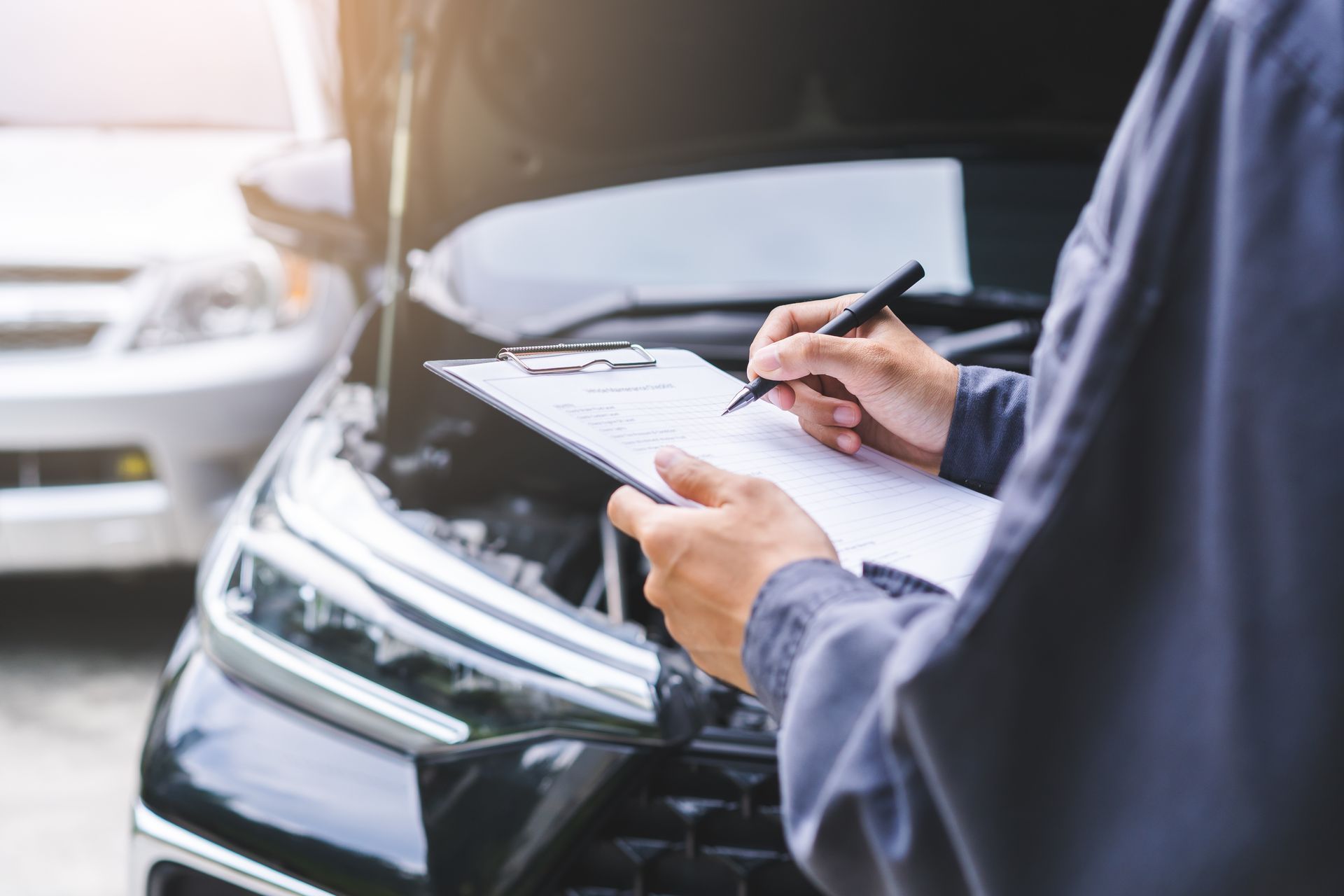Une personne remplit un bloc-notes à côté d'une voiture noire dont le capot est ouvert.