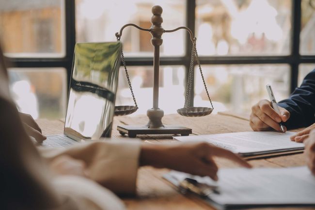 Dos personas están sentadas en una mesa con una balanza de la justicia en el fondo.
