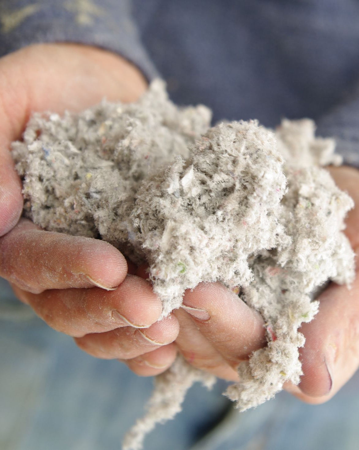 Des mains tenant un tas d'isolant gris.