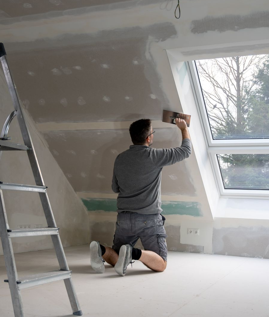 Une personne à genoux applique de l'enduit à plaques de plâtre sur un mur.