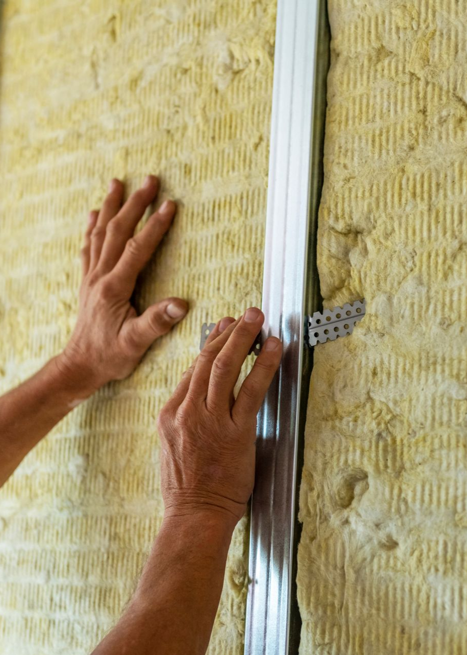 Des mains installent les montants métalliques et l'isolant entre les montants muraux.