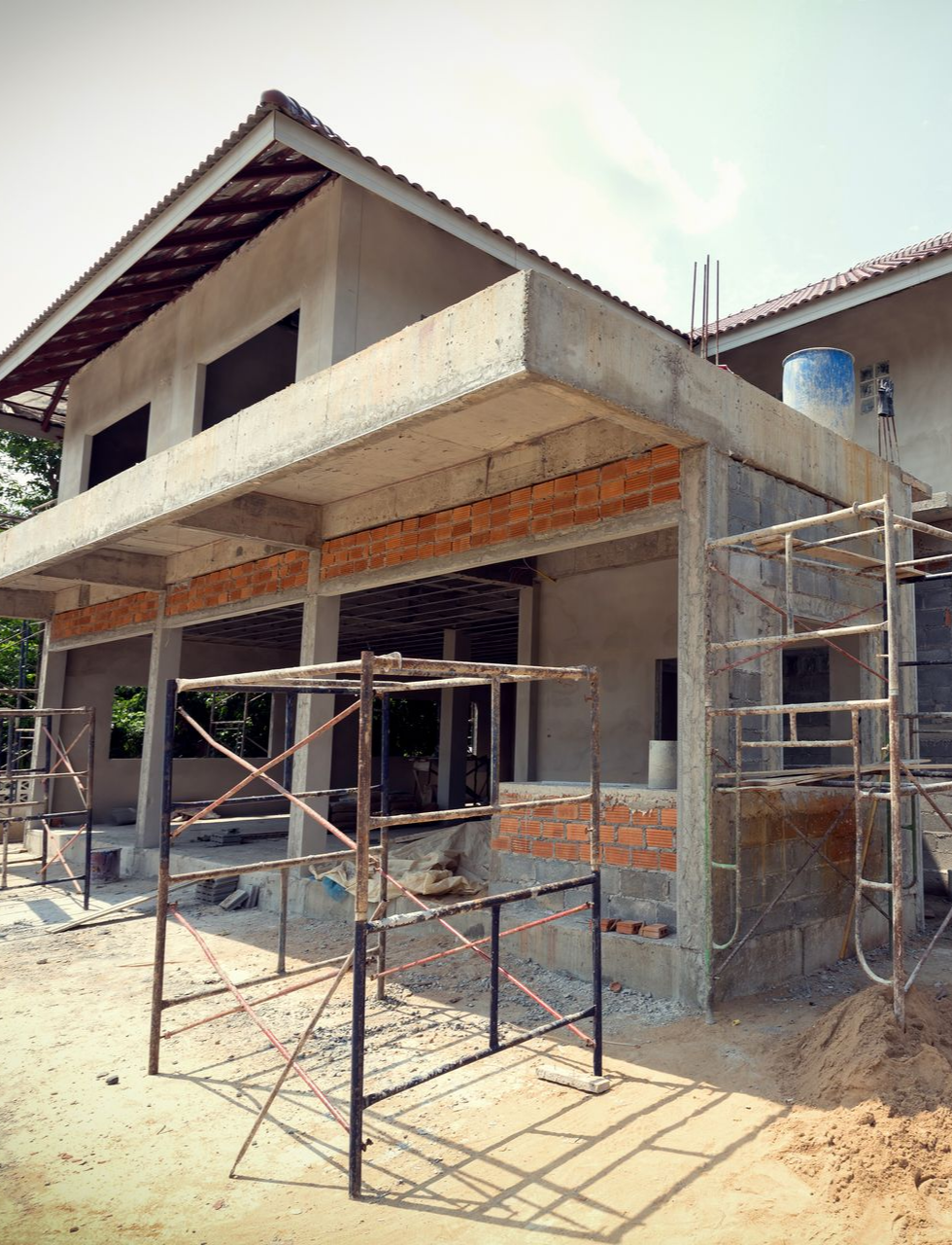 Construction d'un bâtiment à deux étages avec un porche, entouré d'échafaudages et de matériaux de construction.
