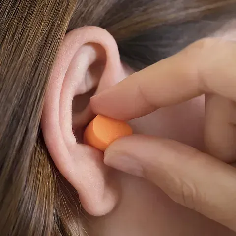 Una persona se pone un tapón naranja en el oído.