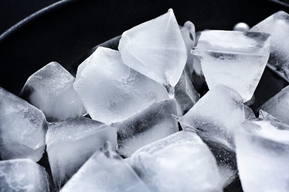 Un recipiente negro lleno de cubitos de hielo sobre una superficie negra.