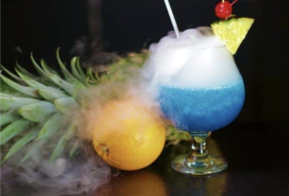 Un cóctel azul con una rodaja de piña y una cereza encima.