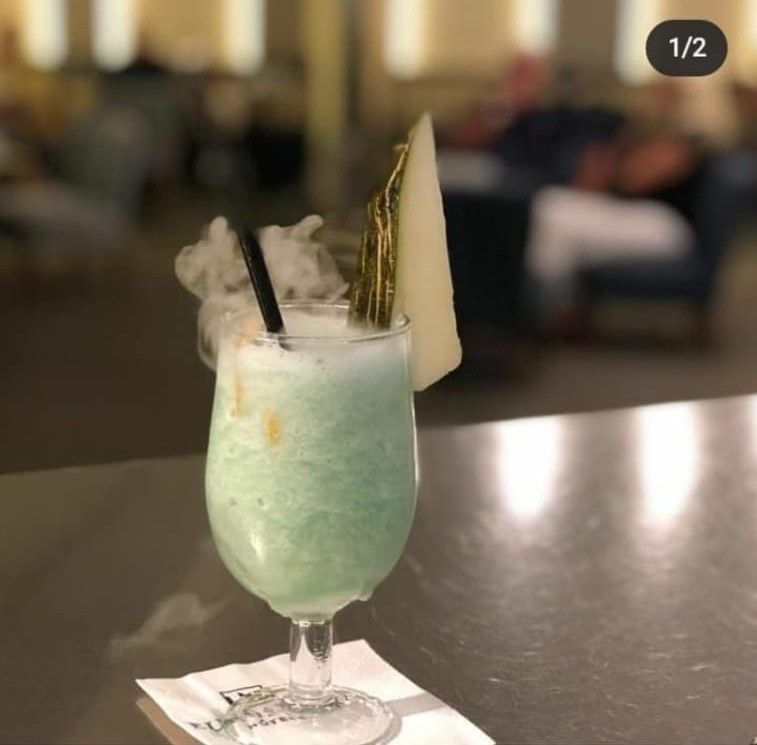 Una bebida en una copa de vino con una pajita y una rodaja de melón encima.