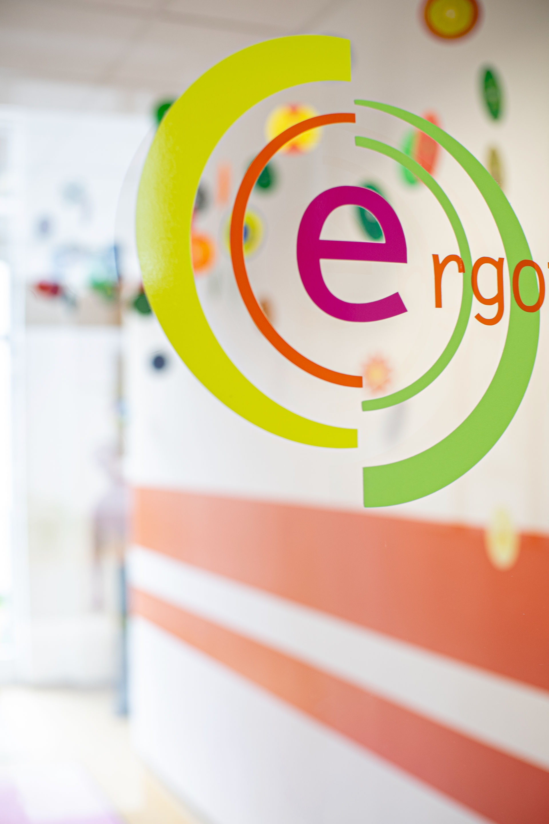 Logo „ergo“ auf der Glastür, bunte Ringe um den Text, orange und weiße Streifen an der Wand.