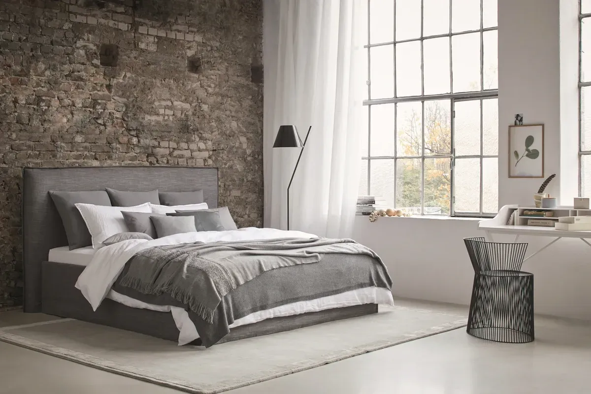 In der Mitte des Zimmers mit der Ziegelwand steht ein Bett.