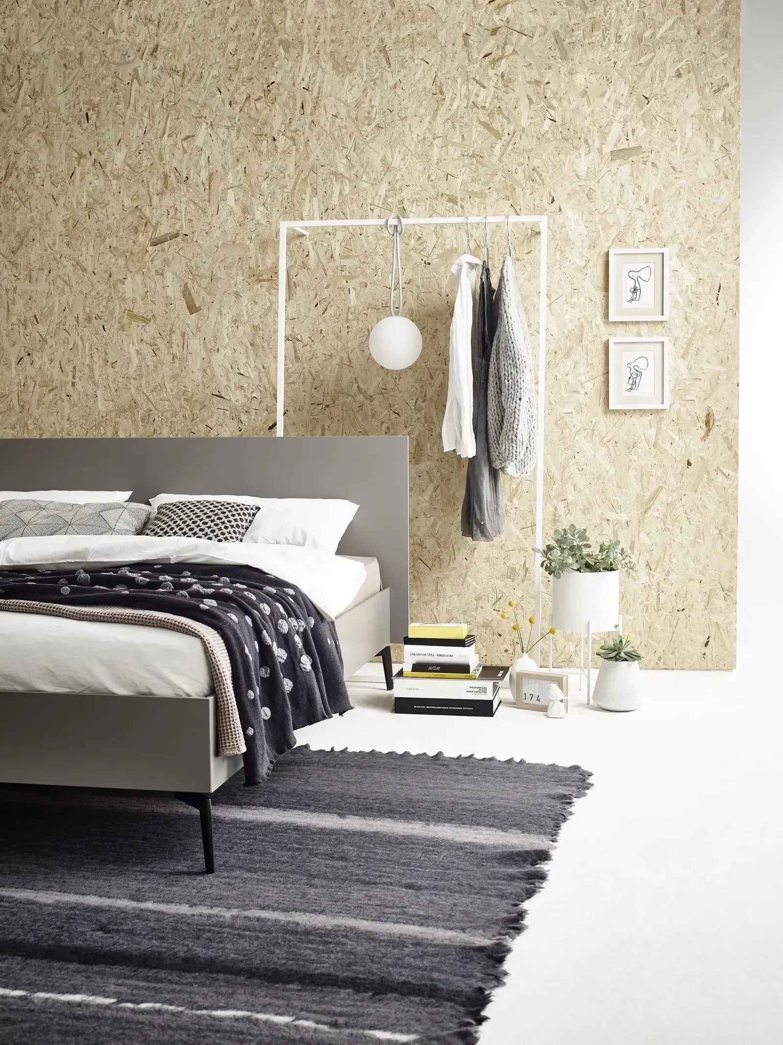 Ein Schlafzimmer mit Bett, Teppich, Kleiderständer und Holzwand.