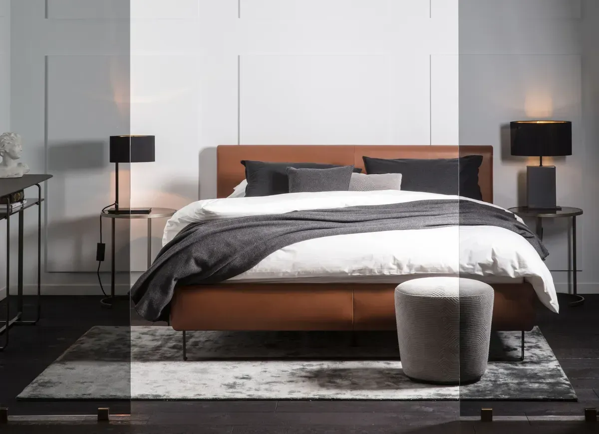 Ein Schlafzimmer mit einem Bett, einem Ottomanen, Lampen und einem Teppich.