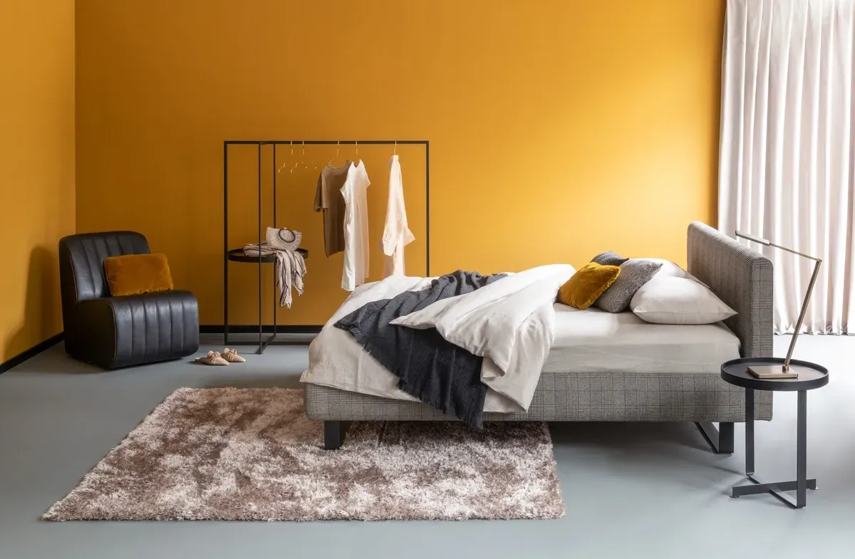 Ein Schlafzimmer mit gelben Wänden, einem Bett, einem Sessel und einem Teppich.